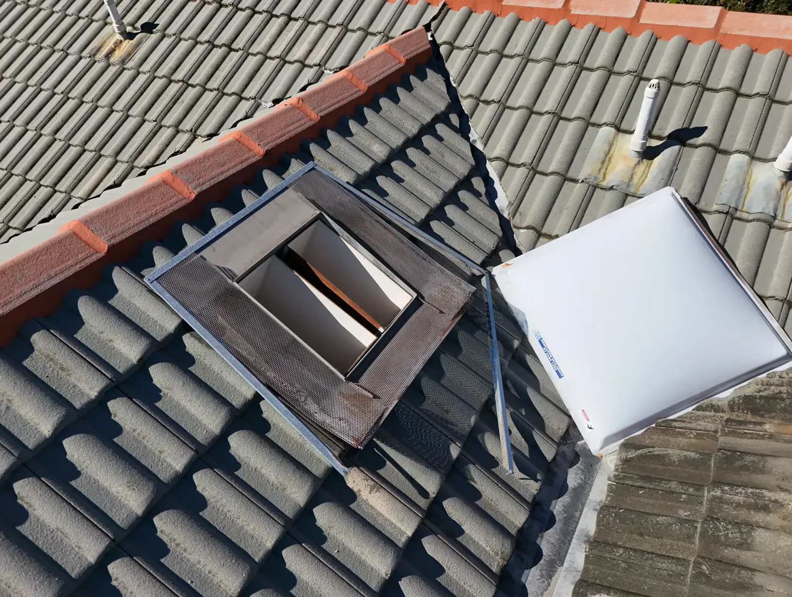 Tiled roof with roof penetrations, ridge capping and a roof-mounted glazed unit